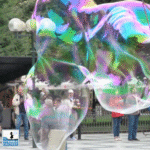 Una bolla di sapone gigante, trasparente con riflessi arcobaleno, che occupa l’intera inquadratura fotografica.